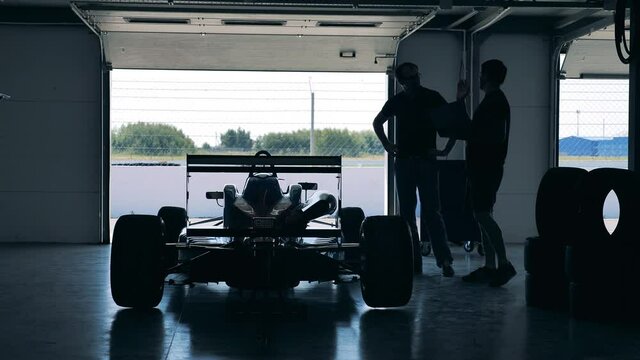 Racing car parked inside of a garage with two mechanics