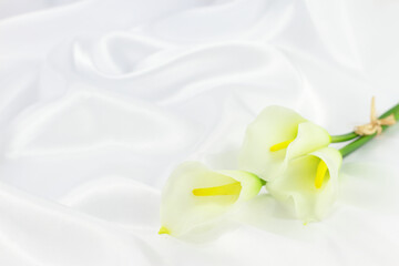 Obraz na płótnie Canvas White calla flowers, Calla lilly flowers on white silk background, copy space 