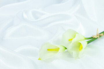 White calla flowers, Calla lilly flowers on white silk background, copy space  - obrazy, fototapety, plakaty