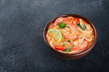 Tom yum noodle soup with spices and shrimp on a dark background.