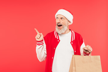Fototapeta na wymiar excited middle aged man pointing with finger and holding shopping bag isolated on red