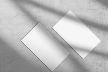 Two empty white rectangle a4 poster, business card or flyer mockups lying diagonally with abstract window shadow overlay on trendy gray concrete background.