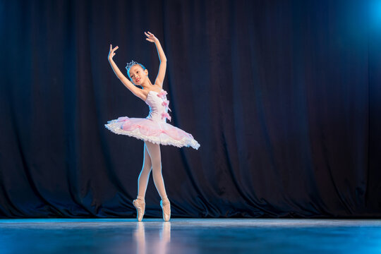 Fototapeta little girl ballerina is dancing on stage in white tutu on pointe shoes classic variation.