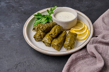 Traditional dish dolma or sarma, with parsley, saucepan with sour cream and lemon in black plate on dark wood background with linen napkin
