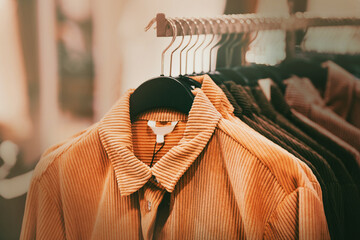 Beautiful corduroy coats for the autumn season in ginger and brown colors hang on hangers in a...