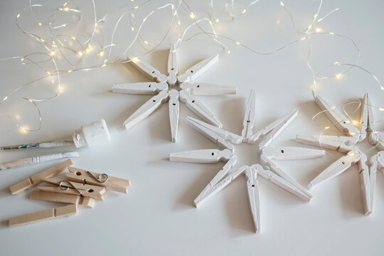 Top view of wooden snowflakes from clothespins painted with white color, recyclable Christmas ornament, New Year DIY decoration, monochrome photography, selective focus on craft
