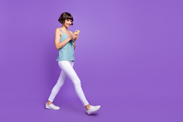 Fototapeta na wymiar Full length body size view of attractive cheery girl walking using device chatting isolated over bright purple violet color background