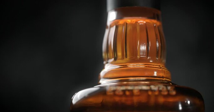 Close up shot of the bottle of whiskey that is spinning around on the dark background, 4k 60p Prores HQ