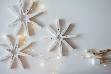 Top view of wooden snowflakes from clothespins painted with white color over white background,...