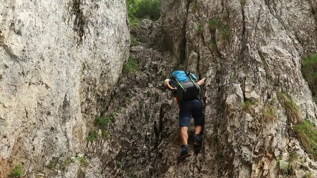 A single hiker with a backpack climb a mountain cliff 