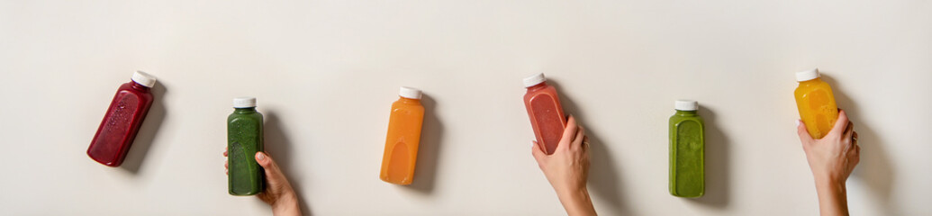 Human hands holding fresh juices in bottles, wide composition