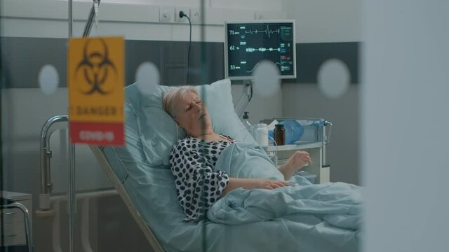Woman with coronavirus symptoms asking for medical help while breathing heavily in hospital ward lockdown. Elder patient in isolated area against virus laying in bed and hyperventilating