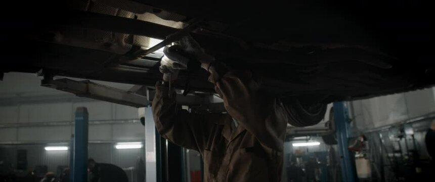CU portrait of Caucasian female mechanic repairing a car in a workshop, working under car bottom. Shot with 2x anamorphic lens