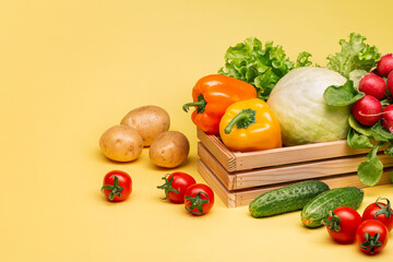 Harvest of vegetables. Potatoes, radishes, cabbage, cucumbers, lettuce leaves, peppers, on a bright yellow background in a wooden box. Copy space. Healthy eating.