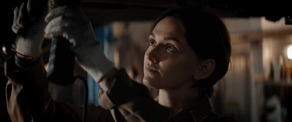 CU portrait of Caucasian female mechanic repairing a car in a workshop, working under car bottom. Shot with 2x anamorphic lens - Powered by Adobe