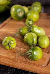 Vertical image.Wooden cutting board and fresh juicy unripe tomatoes on it