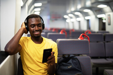 Young man travel by train. Handsome african man listening the music while travel..