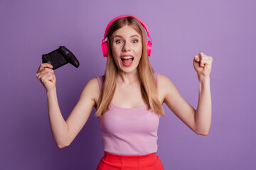 Obraz na płótnie Canvas Portrait of cheerful astonished champion lady hold joystick open mouth wear headphones pink top on purple background