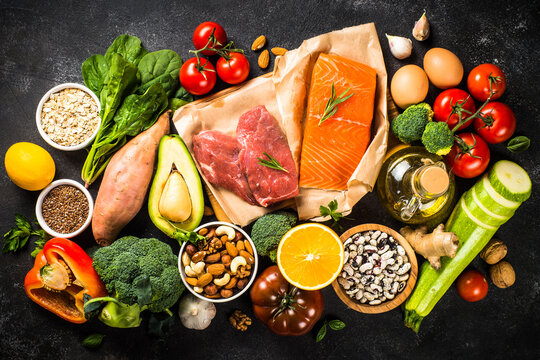Healthy food products. Balanced nutrition. Salmon fish, beef, beans, nuts and vegetables with olive oil. Top view image at black stone table.