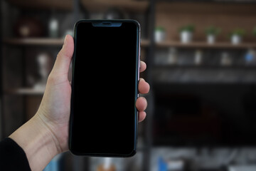 Hand held black phone with a blank screen in the office in the morning light.