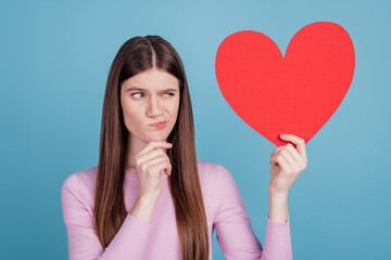Photo of pretty girl think hmm doubt look big paper heart valentine day feelings isolated over blue color background