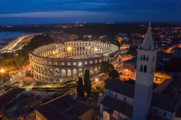 An aerial view of Pula aphitheatre by night, on right side bell tower of St. Antun church, Istria, Croatia