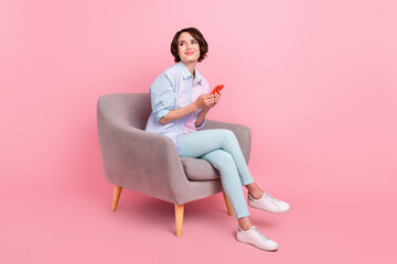 Fototapeta na wymiar Full length body size photo woman sitting browsing internet on smartphone looking copyspace isolated pastel pink color background