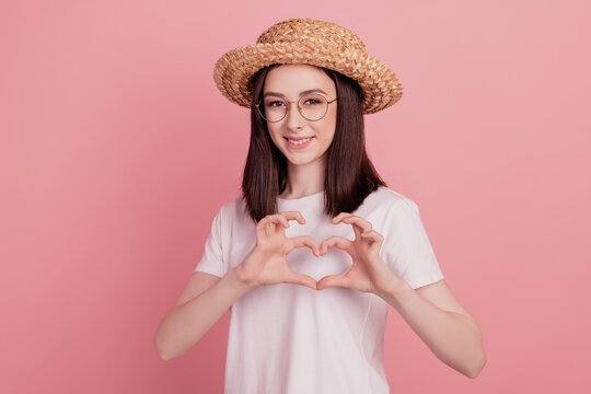 Photo of young attractive girl happy positive smile sunhat vacation show fingers heart symbol isolated over pink color background - Powered by Adobe
