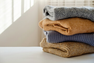 Bunch of knitted warm pastel color sweaters with different knitting patterns folded in stack, clearly visible texture. Stylish fall-winter season knitwear clothing. Close up, copy space for text.