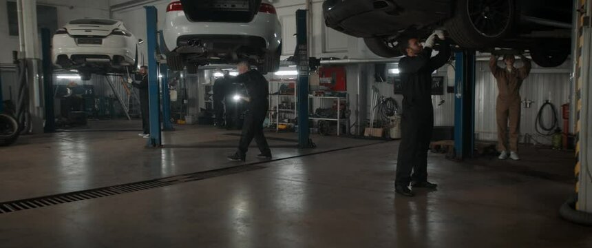 WIDE Team of mechanics wearing overalls doing some car repairs in a workshop. 50 FPS slow motion. Shot with 2x anamorphic lens