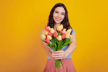 Portrait of a happy young attractive girl holding tulips birthday party isolated over yellow color background