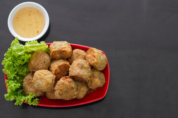 Top view of Deep Fried Crab Meat Rolls or Thai name is Hoi Jo in red plate with vegetables and  plum sauce on black table.