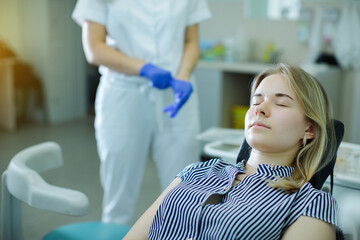 Obraz premium the patient, lying in the dental chair, waits for the dentist to come up to the chair and putting on gloves