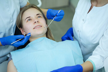 the dentist doctor with the help of dental instruments manipulates the teeth of a smiling patient, lying in the dental chair. the assistant is nearby.