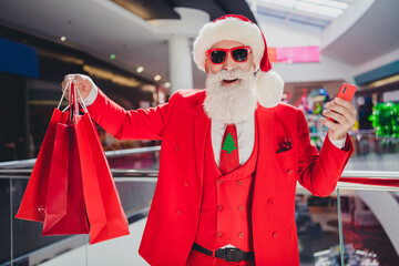 Photo of popular santa hold phone prepare x-mas presents wear sunglass hat red tux in supermarket mall center