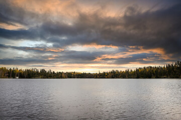 Sun rise lighting up vibrant cloudy sky with variety of lush forest colors below along lake side.