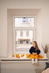 Cheerful Little cute girl with tangerines sitting on window at home