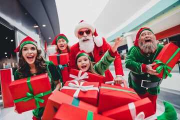 Fototapeta premium Photo of excited lucky santa claus assistants wear costumes smiling rising fist buying many gift packages indoors shopping center