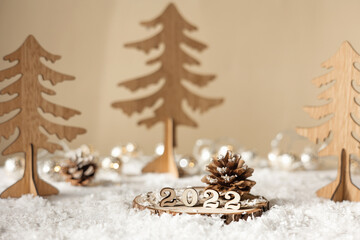 Fototapeta na wymiar New year 2022. Numbers 2022 on wooden stand on beige pastel blurred background with decorative fir trees, snow and lights. Christmas greeting card.