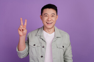 Photo of friendly cheerful korean man show v-sign isolated violet color background