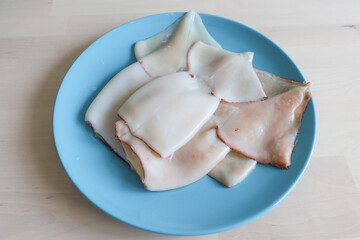 the squid carcass lies on a plate on the table. Proper nutrition, protein, seafood, affordable squid meat, raw food diet