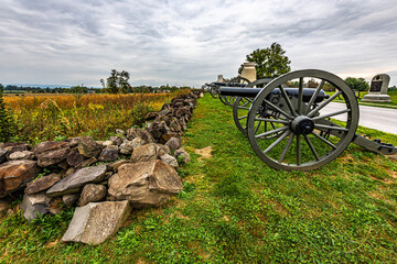 Civil War cannons in front of stone wall and colorful field in the autumn 