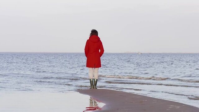 A Woman in a Red Jacket Looks at the Foamy Waves. Windy Autumn Day at the Shore of Lake Ilmen. Northern landscape