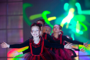 Fototapeta premium Little girls are performing a dance number. Dance for Helovinna in red suits. Girl dancing. Emotional performance of a children's dance group.