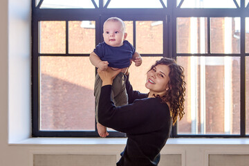 Fototapeta na wymiar Smiling woman is holding little boy in hands indoors.