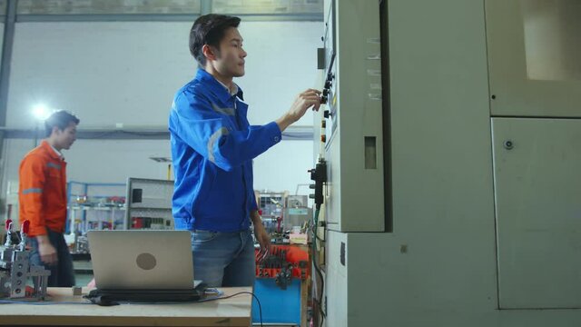 Co-working technician asian male engineer standing hand use laptop application result report discuss for quality control production line of cnc machine operate metal cutting work smart technology 