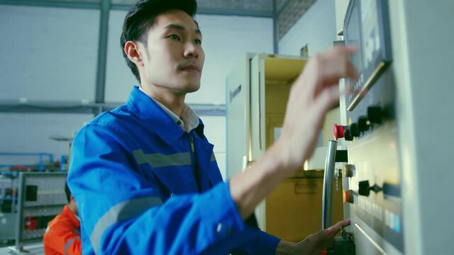 Co-working technician asian male engineer standing hand use laptop application result report discuss for quality control production line of cnc machine operate metal cutting work smart technology 