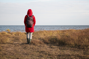 A Woman in a Red Jacket Looks at the Foamy Waves