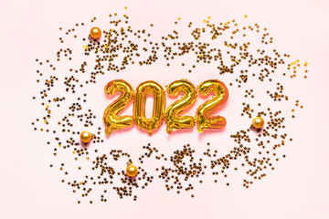 Sparkling gold stars and gold foil balloons 2022 on pink background. Magic Christmas confetti sparkles. Holiday concept