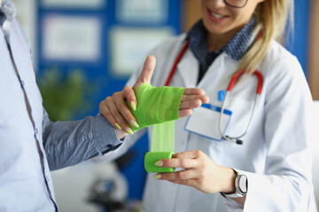 Doctor bandaging wound on patient arm with green bandage in clinic closeup